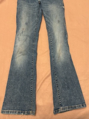 Blå h&m bootcut jeans med slitningar 146 - Ett par blå bootcut jeans med snygga slitningar och ljusa tvättade partier. Klassisk femficksmodell med dubbla knappar i midjan och bälteshällor. Jeansen har en avslappnad passform och är tillverkade i denim.