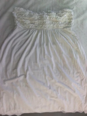 Vit klänning från Victoria`s Secret - Supersött vit klänning eller nattlinne från Victoria's Secret med volangdetaljer upptill och axelbandslös design. Med knytband där bak. Mjukt och lätt material som känns skönt mot huden, perfekt för mysiga kvällar hemma eller varma sommardagar.