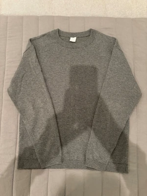 Grå stickad tröja i basic stil - En enkel och stilren grå stickad tröja med rund halsringning och långa ärmar. Tröjan har ribbade muddar vid ärmslut, hals och nederkant. Perfekt för lager på lager och passar till det mesta i garderoben.