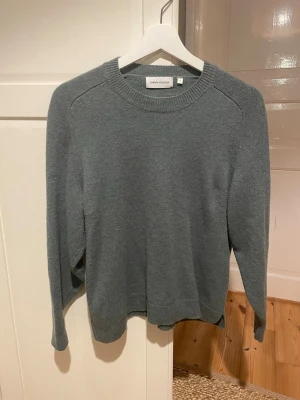 Grön stickad tröja Carin Wester - Mysig grön stickad tröja från Carin Wester med rund halsringning och långa ärmar. Tröjan har en enkel och stilren design med ribbade muddar vid hals, ärmslut och nederkant. Perfekt för lager på lager och passar till det mesta.