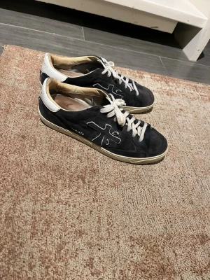 Mörkblå Premiata sneakers med vit sula - Snygga mörkblåa sneakers från Premiata med vit sula och vita skosnören. Skorna har en låg profil och detaljer i mocka samt en kontrasterande vit hälkappa. Klassisk design med logga på sidan och bekväm gummisula.