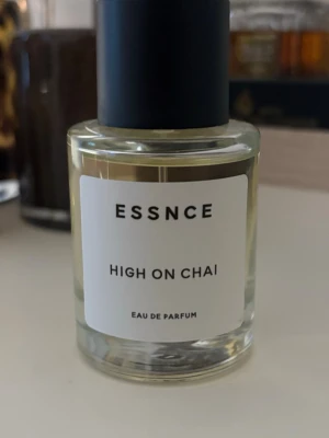 ESSNCE High On Chai Eau de Parfum - ESSNCE High On Chai Eau de Parfum kommer i en stilren, rund glasflaska med svart lock och vit etikett. Doften har en ljusgul vätska och flaskan har minimalistisk design som känns modern och trendig.