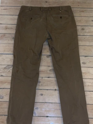 Bruna chinos med raka ben - Säljer ett par bruna chinos med raka ben och klassisk passform. Byxorna har bälteshällor, två bakfickor med knapp och är tillverkade i ett mjukt bomullsmaterial. Perfekta för en avslappnad men ändå stilren look.