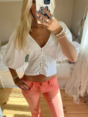 Vit blus med puffärm och knappar - Superfin vit blus med puffiga ärmar och v-ringning. Toppen har knappar framtill och är croppad, vilket ger en trendig look. Perfekt till jeans eller kjol för en snygg outfit.
