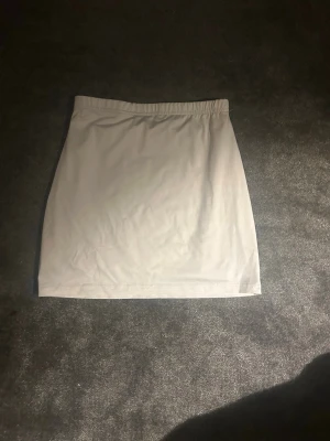 Vit kortkjol med enkel design - Säljer en vit kortkjol med rak passform och resår i midjan. Kjolen är enkel och stilren, perfekt att matcha med olika toppar. Materialet känns mjukt och stretchigt vilket gör den bekväm att bära.