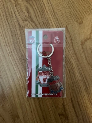Liverpool FC nyckelring metall - Snygg nyckelring i metall med Liverpool FC:s klassiska klubbmärke i rött, vitt och grönt. Perfekt accessoar för dig som älskar fotboll och vill visa ditt stöd för The Reds. Nyckelringen har en robust ring och kedja.