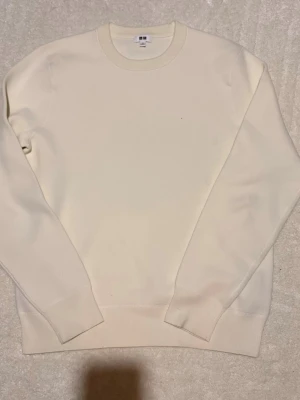 Krämvit sweatshirt från Uniqlo - En stilren krämvit sweatshirt från Uniqlo med rund halsringning och ribbade muddar vid ärmslut och nederkant. Tröjan är enkel och clean i designen, perfekt för en minimalistisk look. Tillverkad i mjukt material som känns skönt mot huden. Helt oanvänd!!