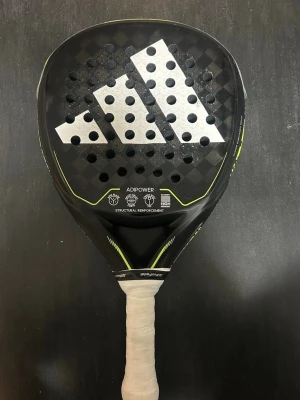 Adidas Adipower padelracket - Säljer ett Adidas Adipower padelracket i svart med stora vita och gula detaljer. Racketen har rund form, perforerat slagblad och vit lindad greppyta. Tillverkat i kolfiber med strukturell förstärkning för extra kraft och kontroll.