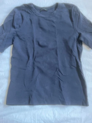 Mörkblå basic t-shirt från Zara - En enkel och stilren mörkblå t-shirt från Zara. Modellen har rund halsringning och korta ärmar. Perfekt att matcha med jeans eller kjol för en clean look. Tillverkad i mjuk bomull som känns skön mot huden.