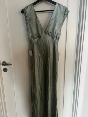 Lång grön omlottklänning i satin - Snygg långklänning som är helt ny med lapparna kvar. Perfekt till balen eller sommarens fester! Hör av dig vid frågor!☺️