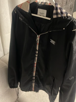 Burberry windbreaker  - Säljer min svarta Burberry-jacka som jag tyvärr inte använder längre. Lätt och smidig jacka med huva och det klassiska Burberry-mönstret på insidan. Den är justerbar nertill så man kan dra åt den efter hur man vill ha passformen.                                                                   Den är i storlek M men kan även passa S och L.                                    Skriv gärna till mig vid eventuella frågor eller prisförslag Mvh Seller😊