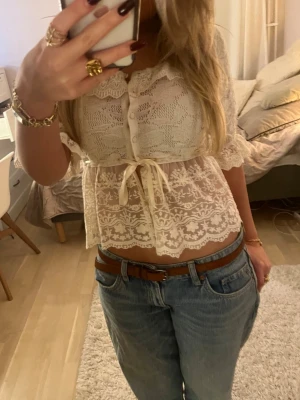 Vit spetsblus med knappar och rosett - Supersöt vit blus i spets med knappar framtill och en rosett i midjan. Den är supersött från zara med trekvartsärm och spetsdetaljer🩷