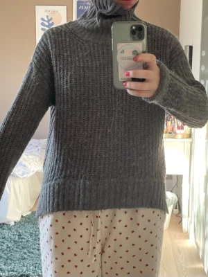 Grå stickad polotröja från 157 - Mysig grå stickad polotröja från 157 med grovstickad struktur och hög krage. Tröjan har långa ärmar och bred ribbad kant nedtill och vid ärmslut. Perfekt för kalla dagar och enkel att matcha med olika outfits.