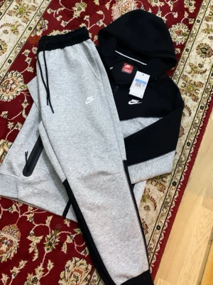 Nike hoodie svart och grå - Snygg hoodie från Nike i svart och grått med dragkedja och huva. Klassisk Nike-logga på bröstet och praktiska fickor med dragkedja. Perfekt för en sportig och avslappnad stil. Tillverkad i mjukt och bekvämt material.