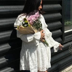 VIT KLÄNNING - Säljer denna sommardrömmen!! En superfin vit kortklänning med voluminösa långa ärmar och subtilt blommönster i tyget. Klänningen har en lös passform, samt volangdetaljer vid ärmslut och kjol. Perfekt för sommarens alla tillfällen! St 40/38. Den passar mig som har s/m💕använd endast en gång<3