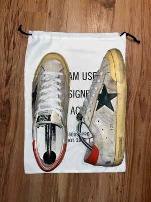 Golden Goose - Superstar - Selling these rare Golden Goose (GGDB) Superstars in a very clean used look. They come with eyecatching orange and green details and offer real comfort. Size 43. Really good condition. Only flaw is a little use on the heel, which is usual on these type of soles. I’ve glued them for extra hold (pic 7). Box and dustbags follow. Feel free to ask any questions for further pictures, measurements or bids!
