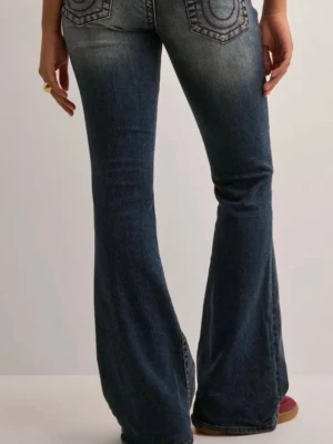 Bootcut jeans från True Religion - Snygga blå bootcut jeans från True Religion med ikoniska bakfickor och röda kontrastsömmar. Jeansen har en klassisk femficksdesign och en patch med logga bak i midjan. Perfekta för dig som gillar en retro och avslappnad stil.