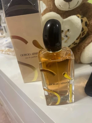 Giorgio Armani Eau de Parfum - Elegant parfym från Giorgio Armani i en stilren glasflaska med svart kork och guldiga detaljer. Doften kommer i en exklusiv förpackning med guldmönster och rymmer 100 ml. Perfekt för dig som vill ha en lyxig och tidlös signaturdoft.