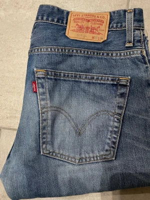 Levi's 507 blå raka jeans - Klassiska blå Levi's 507 jeans med raka ben och femficksmodell. Jeansen har den ikoniska röda Levi's-lappen på bakfickan och patch i läder bak i midjan. Tillverkade i slitstark denim som ger en tidlös look. Storlek 31/32 