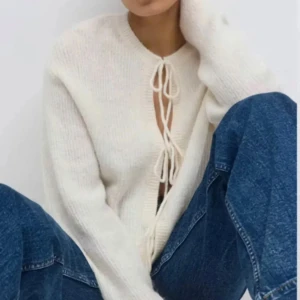 Vit stickad kofta med snörning - Säljer en stilren vit stickad kofta med knytband framtill. Koftan har långa ärmar och en mjuk, bekväm passform. Perfekt för lager-på-lager under kyligare dagar. Helt ny med lappen kvar, då den bara hängt i garderoben.