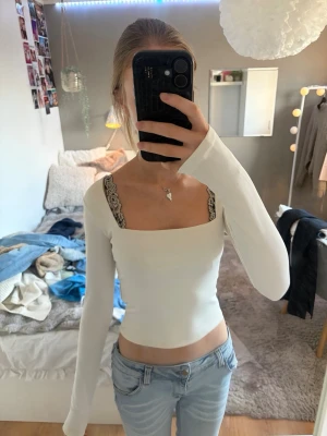 Vit långärmad croppad topp - Säljer en vit långärmad croppad topp med fyrkantig halsringning. Toppens material är mjukt och stretchigt, perfekt för att matcha med jeans eller kjol. Enkel och stilren design som ger en snygg och modern look.