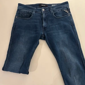 Mörkblå jeans från Replay - Snygga mörkblå jeans från Replay med klassisk femficksdesign och diskreta slitningar. Jeansen har raka ben och silverfärgade detaljer vid fickorna. Perfekta för en trendig och avslappnad stil.
