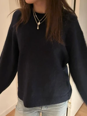 Mörkblå stickad tröja - En enkel och stilren mörkblå stickad tröja med rund hals och långa ärmar. Tröjan har en rak passform och ribbstickade muddar vid ärmslut och nederkant. Perfekt att matcha med jeans för en avslappnad look.