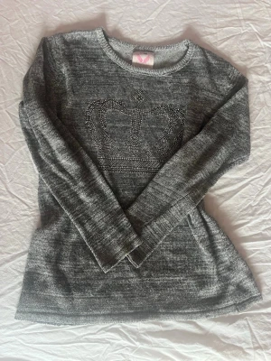 Grå stickad tröja med krona - Snygg grå stickad tröja med ett coolt kronmotiv i silvriga nitar på bröstet. Tröjan har rund halsringning och långa ärmar, perfekt för att hålla sig varm och stilren. Materialet är mjukt och bekvämt, passar dig som gillar enkel men trendig design. 2000s vibe!! Just nj lägger jag ut en del plagg så kolla gärna in det, rabatt vid köp av flera!!💖