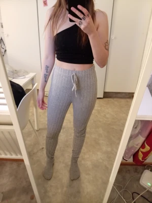 Grå ribbade leggings med knytband - Säljer ett par grå ribbade leggings med hög midja och knytband i midjan. De är mjuka och stretchiga, perfekta för en chill och avslappnad stil. Materialet känns mysigt och leggingsen har en smickrande passform.