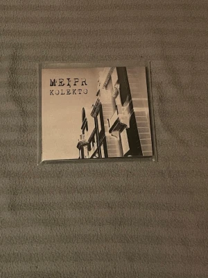 Meipr Kolekto zine/fanzine - Säljer en zine eller fanzine med titeln 'Meipr Kolekto'. Omslaget har ett svartvitt foto av en byggnad och baksidan har en grafisk design med cirklar och figurer. Perfekt för dig som gillar unika trycksaker och samlarobjekt.