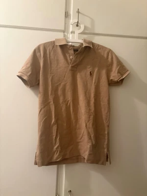 Beige pikétröja från Polo Ralph Lauren - Klassisk beige pikétröja från Polo Ralph Lauren med korta ärmar och krage. Tröjan har en normal passform och är tillverkad i mjuk bomull, perfekt för dig som vill ha en schysstare piké till sommaren. Priset kan diskuteras om ni inte ha pengar