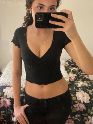 Svart glittrig croppad topp med v-ringning - Säljer en svart, croppad topp med djup v-ringning och korta ärmar. Toppen har en figurnära passform och är tillverkad i ett mjukt och stretchigt material. Den är även lite smått glittrig som passar perfekt till utekvällar och lite festligare outfits