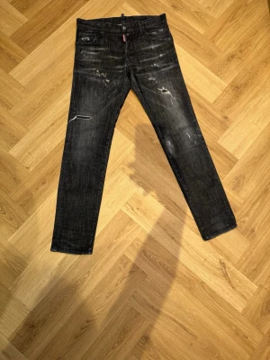 Svarta skinny jeans från Dsquared2 - Säljer ett par svarta skinny jeans från Dsquared2 med slitningar och distressed detaljer. Jeansen har klassisk femficksmodell, knappgylf och smal passform. Materialet är denim i bomull med lite stretch för extra komfort. Modell namn Dsquared2 – Cool Guy Jean. Priset kan diskuteras