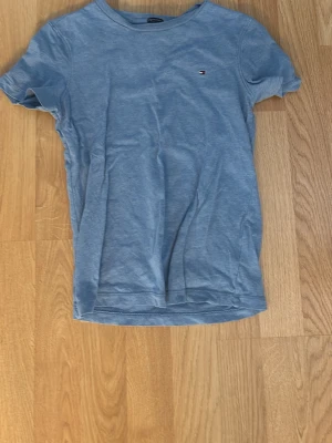 Blå t-shirt från Tommy Hilfiger - Snygg blå t-shirt från Tommy Hilfiger i ekologisk bomull. Klassisk passform med rund hals och liten broderad logga på bröstet. Perfekt till jeans eller shorts för en avslappnad stil.