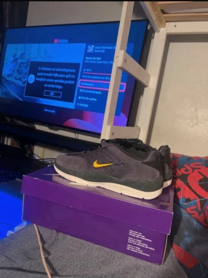 Nike SB Dunk låga sneakers grå/svart - Nike SB Dunk sneakers i grått och svart mocka med gula detaljer och klassisk gul swoosh på sidan. Skorna har en vit och svart sula samt meshpaneler för extra andningsförmåga. Perfekta för dig som gillar streetwear och skatekultur.