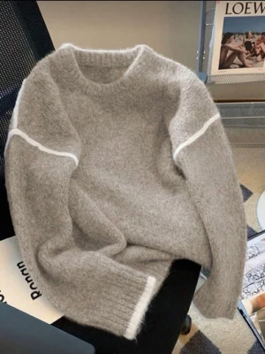 Grå stickad tröja med vita detaljer - Mysig grå stickad tröja med lång ärm och vita ränder över axlarna samt vid ärmslut. Tröjan har en rund halsringning och en avslappnad passform, perfekt för kyliga dagar.