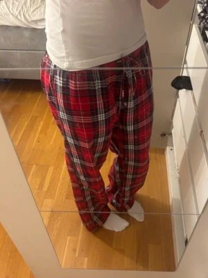 Pyjamasbyxor - Mysiga pyjamasbyxor i rött rutigt mönster med inslag av vitt och svart. Byxorna har en avslappnad passform och justerbar midja med dragsko. Använda fåtal gånger. 