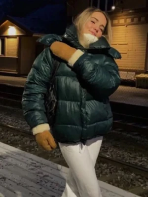 Mörkgrön pufferjacka med hög krage - Säljer en mörkgrön pufferjacka med hög krage och dragkedja framtill. Jackan har ett quiltat mönster och är tillverkad i ett glansigt material som ger en cool look. Perfekt för kalla vinterdagar och håller dig varm och bekväm.