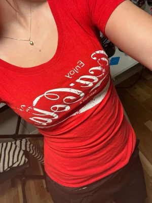 Röd Coca-Cola t-shirt med tryck - Säljer en vintage t shirt som från början var L men som jag sytt ihop i midjan så den är nu tajt som en S/XS. T-shirten har rund halsringning och korta ärmar. Passformen är tight och materialet känns mjukt och stretchigt, troligtvis bomull eller bomullsblandning. Perfekt för dig som gillar retrostil och ikoniska loggor. 