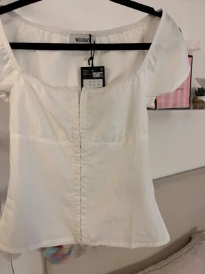 Vit topp med knappar från Weekday - Säljer en söt vit topp från Weekday med korta ärmar och knappar framtill. Toppen har en fyrkantig ringning och är lätt figursydd för en snygg passform. 💓💓