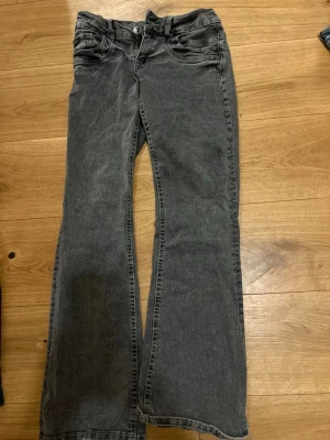 Grå bootcut jeans med låg midja - Säljer ett par grå jeans med bootcut-modell och låg midja. Jeansen har klassiska fem fickor och stängs med knapp och dragkedja. Materialet är denim i bomull och de har en avslappnad passform. Perfekta för en chill och trendig look.