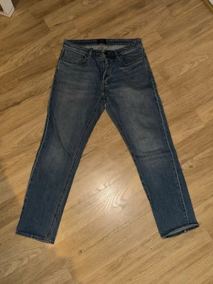 Blå raka jeans från Neuw - Säljer ett par klassiska blå jeans från Neuw med rak passform och knappgylf. Jeansen har fem fickor och är gjorda i ett slitstarkt denimtyg. Perfekta för en avslappnad och stilren look.