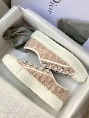 Rosa Dior sneakers med monogram - Snygga sneakers från Dior i beige och vitt med ikoniskt Dior-monogram över hela ovandelen. Skorna har lågt skaft, vita snören och robust vit sula med 'Christian Dior' präglat på sidan. Perfekta för dig som gillar lyxiga detaljer och streetstyle.
