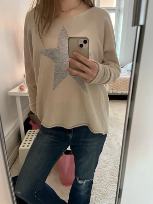 Beige tröja med grå stjärna - Säljer en beige långärmad tröja med en stor grå stjärna på bröstet från Hunkydory Tröjan har avslappnad passform och rund halsringning. Perfekt för dig som gillar en enkel men snygg stil. 