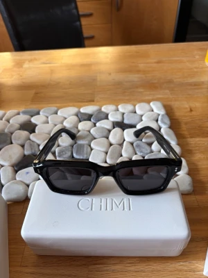 Svarta solglasögon från CHIMI - Snygga svarta solglasögon från CHIMI med rektangulära bågar och mörka linser. Glasögonen har en stilren och modern design, perfekt för dig som vill ha en cool look. Levereras i originalfodral med tillhörande box. Nypris 1350 kr, köpt på NK i Stockholm