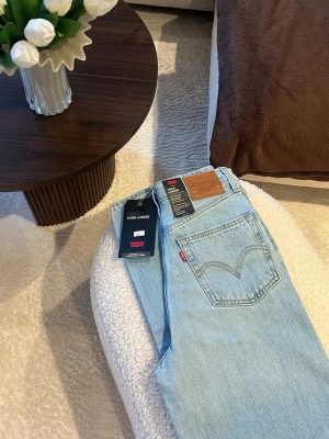 Levi's High Loose ljusblå jeans - Säljer ett par Levi's High Loose jeans i ljusblå denim med hög midja och raka, lösa ben. Klassisk femficksmodell med Levi's ikoniska läderpatch bak och röd logotagg på fickan. Perfekta för en avslappnad och trendig look. Helt nya med prislapp kvar på! 