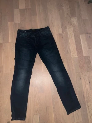 Mörkblå Slim Glenn jeans från Jack & Jones - Säljer ett par mörkblå Slim Glenn jeans från Jack & Jones. Jeansen har en slim fit-modell med klassisk femficksdesign och snygga slitningar på låren. Tillverkade i stretchigt denimtyg för extra komfort.
