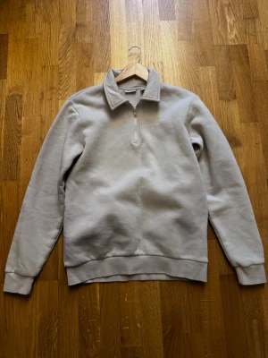 Beige halvzip sweatshirt - Säljer en stilren beige sweatshirt med halvzip och hög krage. Tröjan har långa ärmar, ribbade muddar och är gjord i mjukt, tjockt material som känns riktigt skönt mot huden. Perfekt för dig som gillar en clean och avslappnad look.
