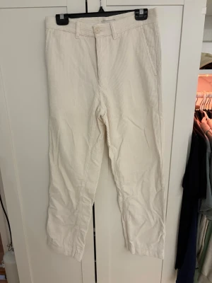 Vita manchesterbyxor These Glory Days - Snygga vita manchesterbyxor från These Glory Days i klassisk rak modell. Byxorna har normal midja, bälteshällor och stängs med knapp och dragkedja. Tillverkade i mjuk manchester som ger en stilren och trendig look.