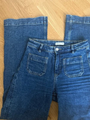 Blå utsvängda jeans från Gina Tricot - Snygga blå jeans från Gina Tricot med utsvängda ben och två stora fickor framtill. Jeansen har medelhög midja och klassisk knappstängning. Perfekta för dig som gillar en retroinspirerad look och vill ha ett par bekväma jeans i mjukt denimtyg. Superbra skick, säljer för de är för långa på mig🩷